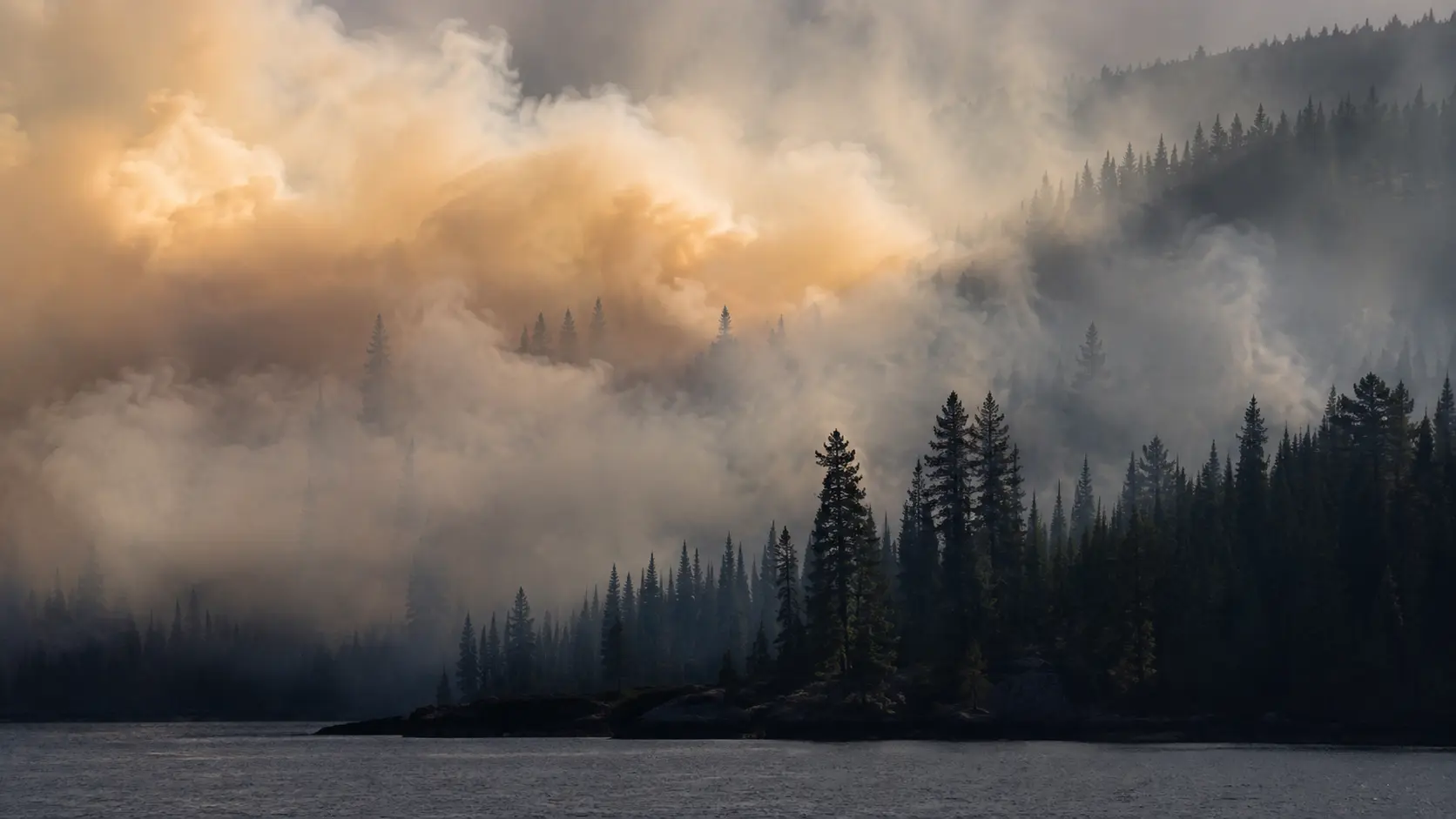 Thick wildfire smoke drifting low over a northern boreal forest and lake shoreline, illustrating the remote terrain firefighters faced in the Boundary Waters