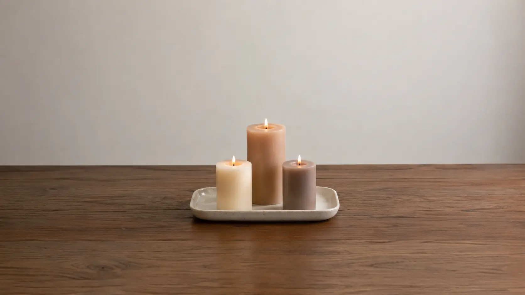 Three candles correctly placed on ceramic tray on coffee table with clear 12-inch space around them away from book stack and plant decoration showing proper safe candle setup