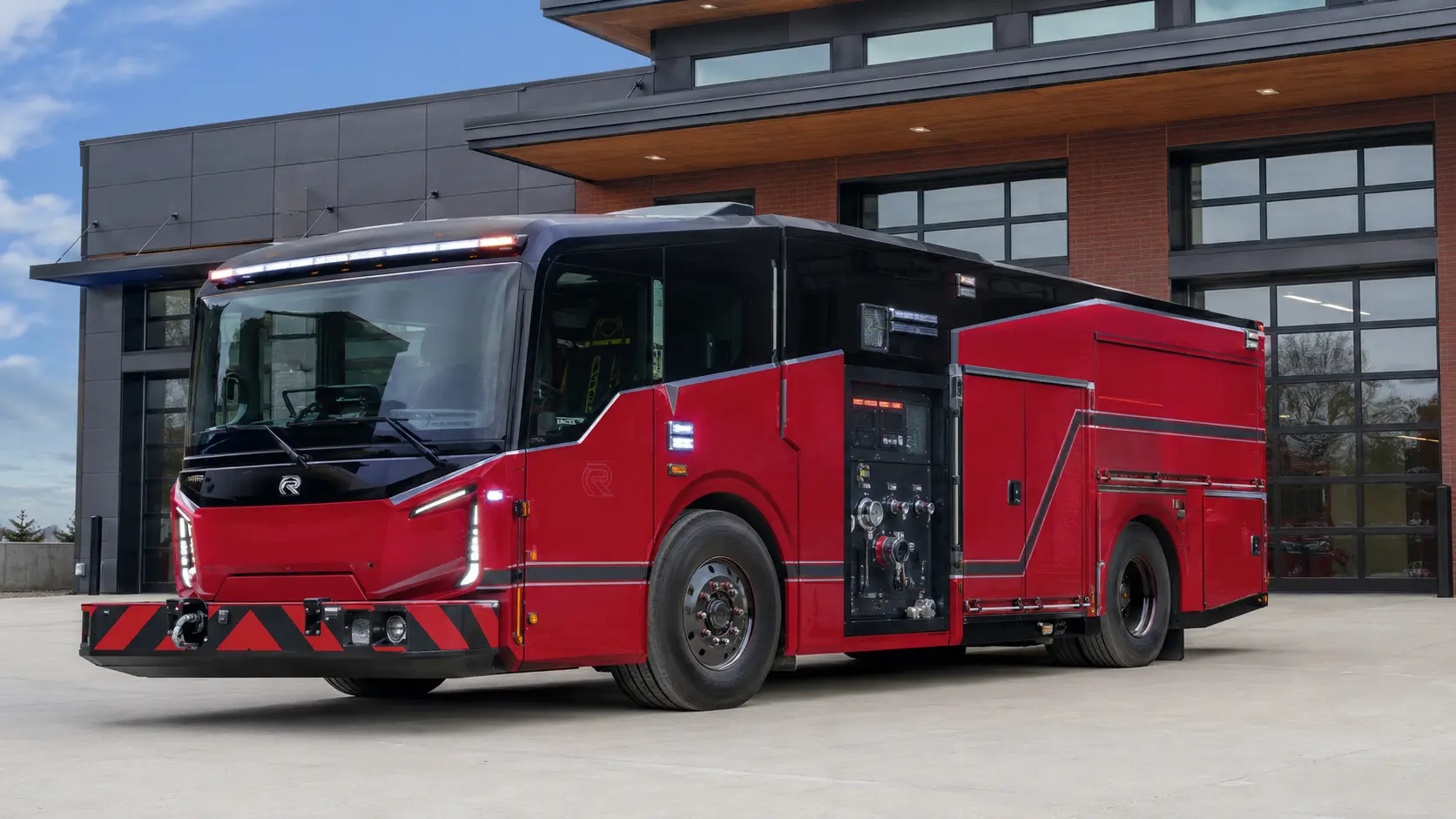 Modern red electric fire engine parked in front of a fire station.