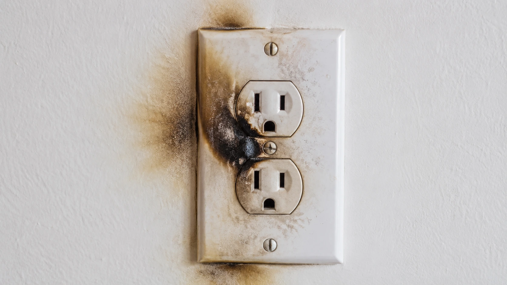 Discolored and scorched electrical outlet cover plate showing burn marks and heat damage &mdash; warning sign of electrical fire risk requiring immediate attention