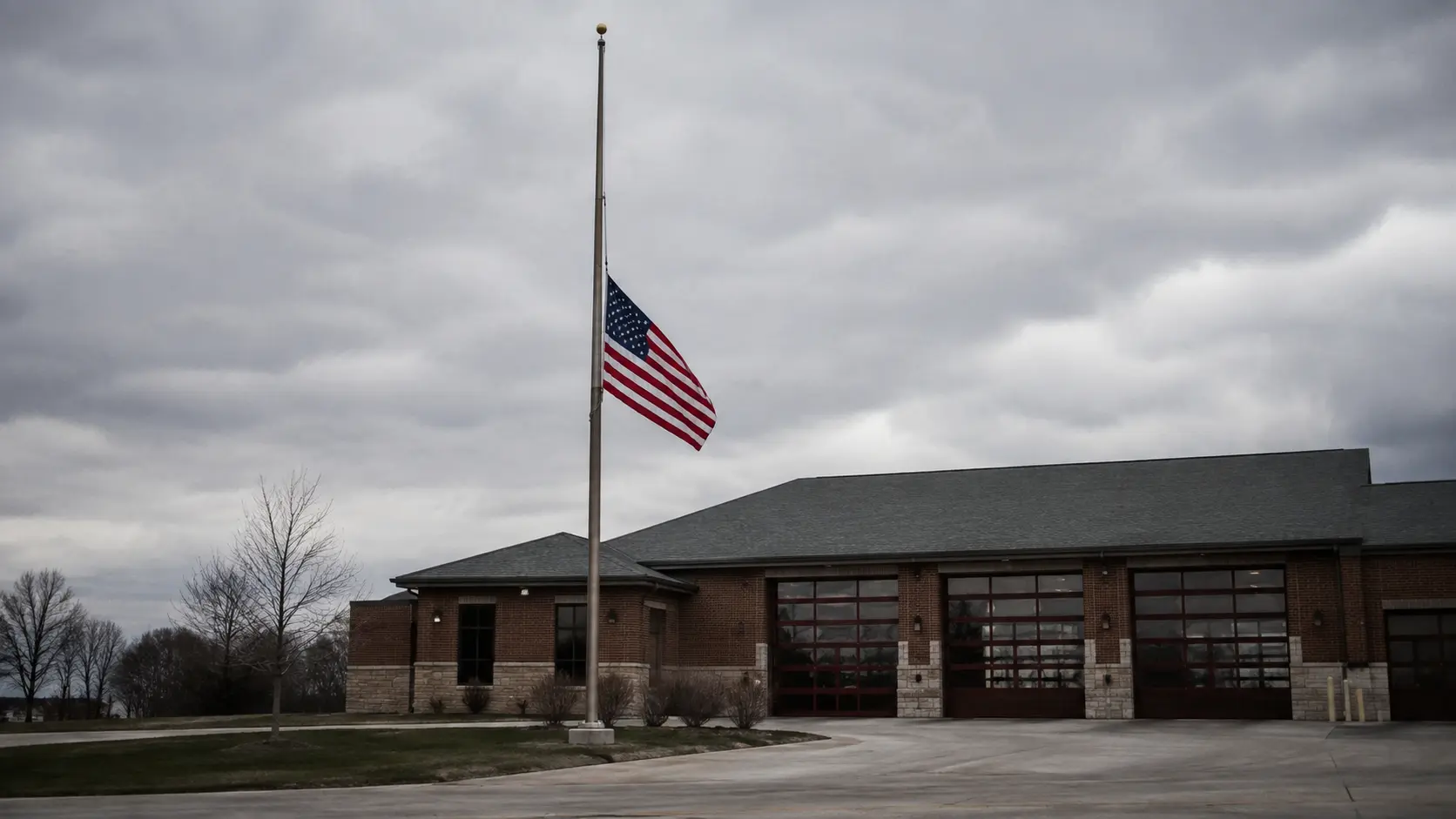 American flag flying at half-staff in front of a fire station, a gesture of respect commonly ordered by cities following a firefighter's line-of-duty death