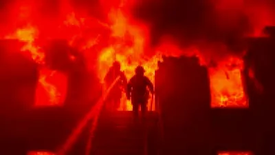 Firefighter battling flames at a North Houston warehouse fire, smoke billowing into the sky.
