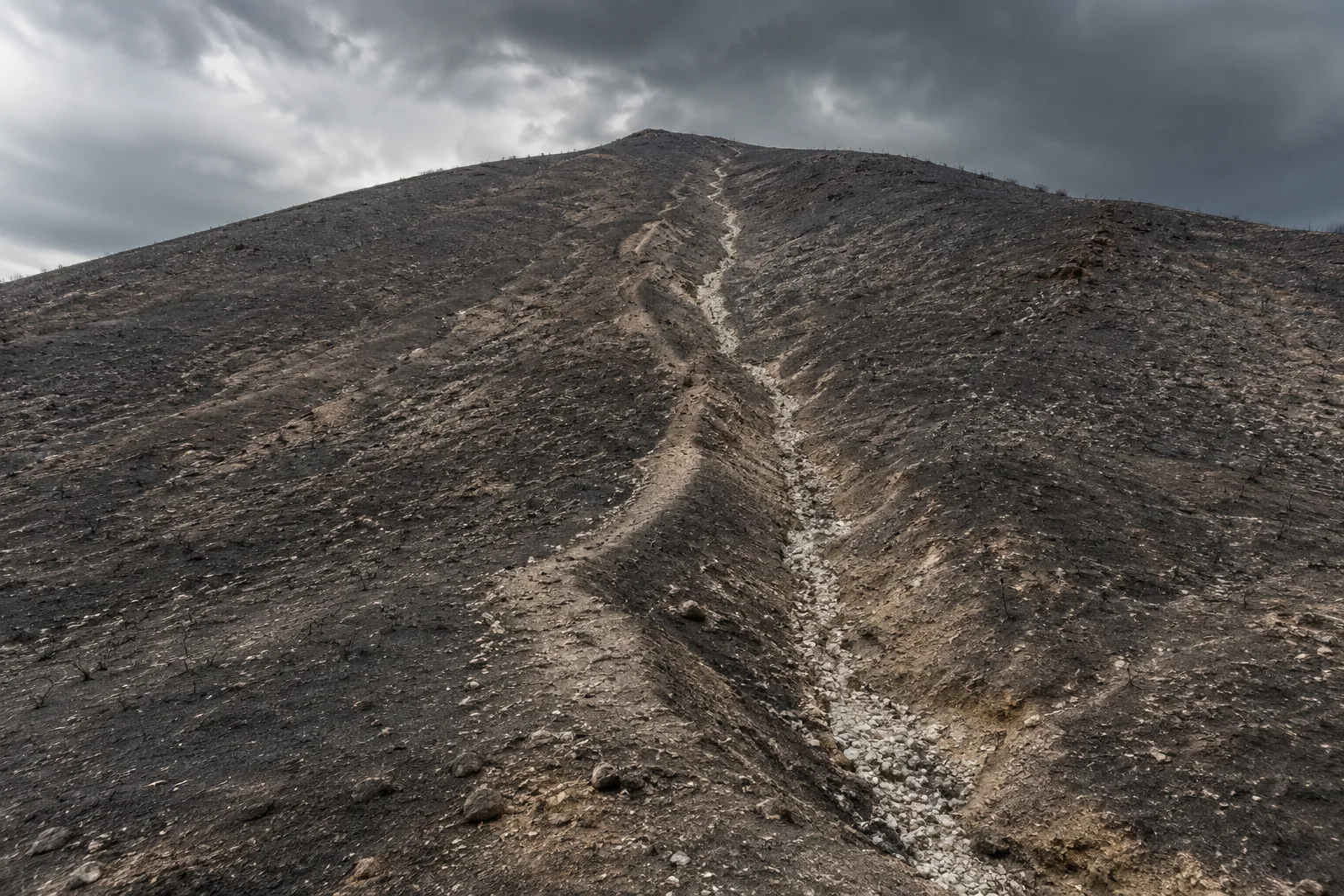 Muddy debris flow water carrying ash and rock down a channel below a burned hillside