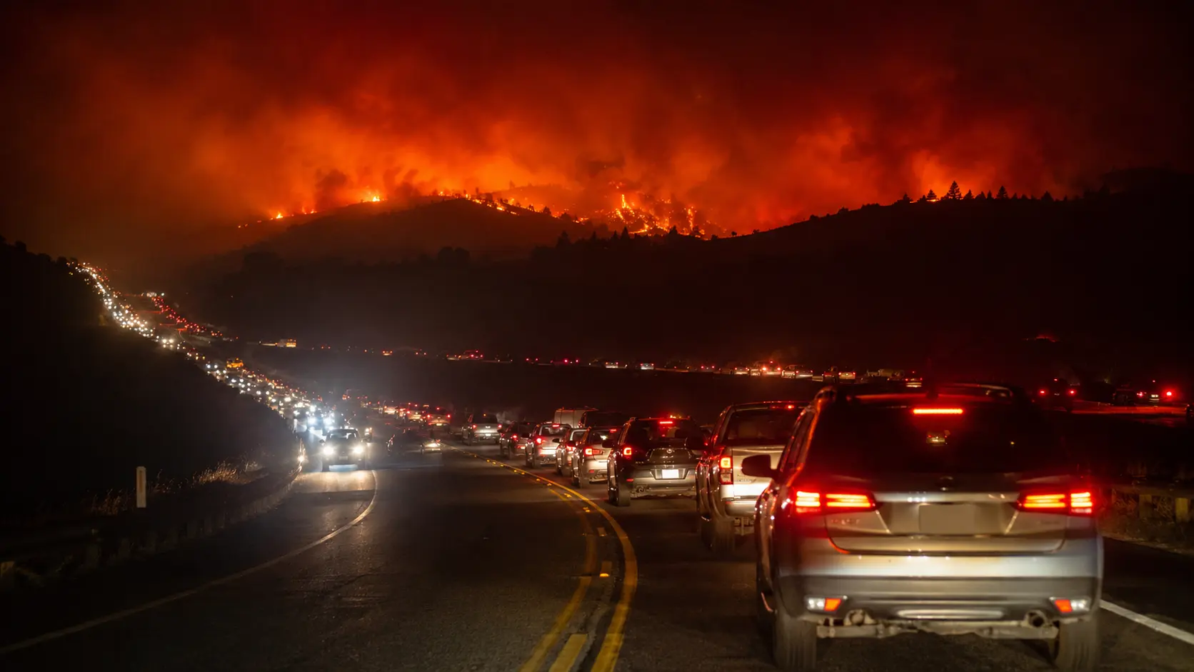 Line of vehicles evacuating along U.S. 395 near Reno, Nevada at night under an orange smoke-filled sky during the Hawk Fire evacuation