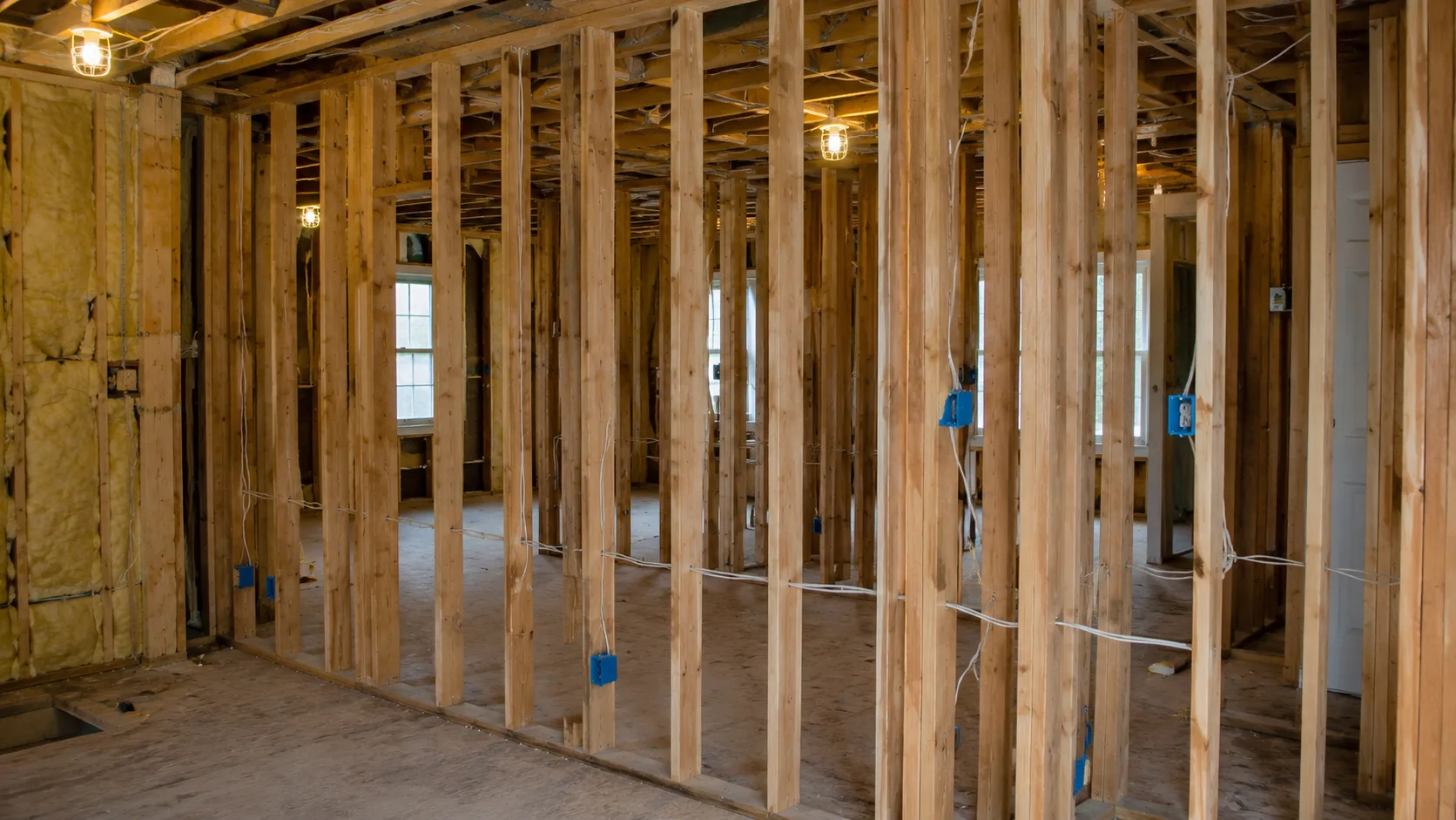 Interior of a home under renovation showing open wall cavities with exposed wood studs and open stud bays running continuously between floors, electrical wiring visible, no drywall or fire blocking present &mdash; illustrating how renovation removes the fire compartmentalization that drywall provides and creates continuous fire pathways through the structure