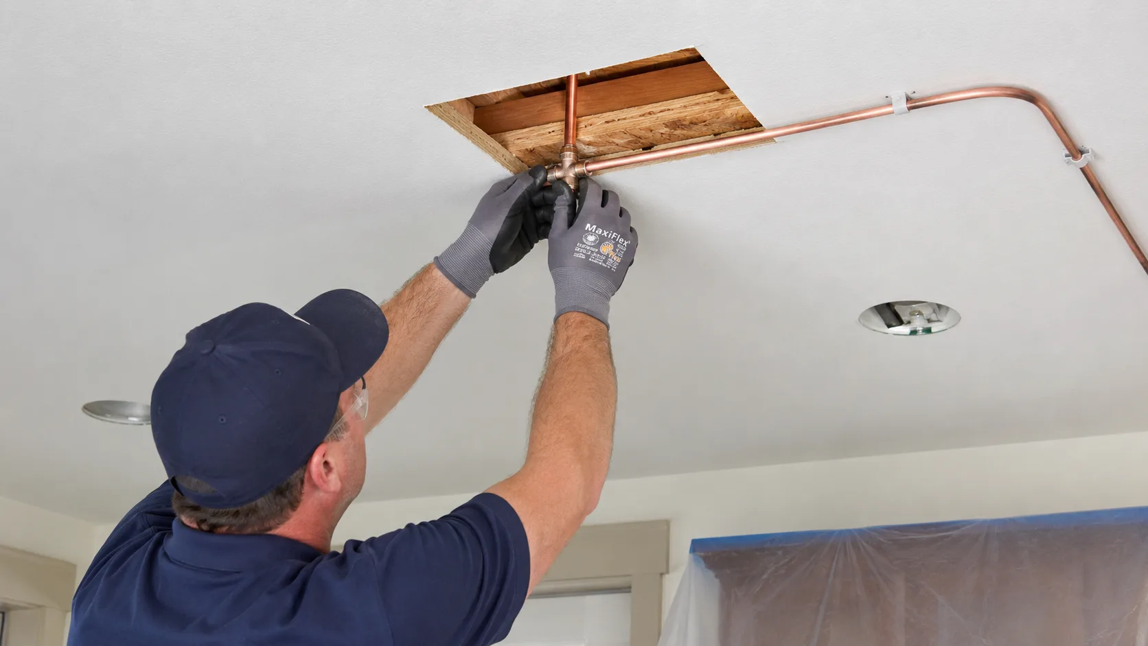 Plumber installing residential fire sprinkler piping in ceiling of existing home during retrofit installation showing pipe routing and head placement