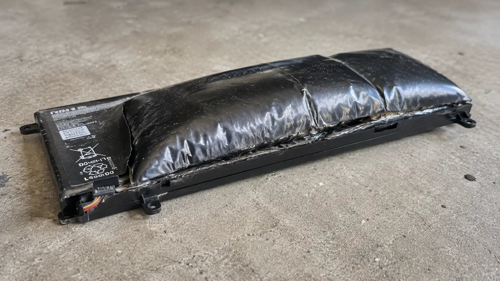 Swollen bulging lithium-ion battery removed from laptop showing dangerous expansion from internal gas buildup &mdash; immediate replacement required, fire risk