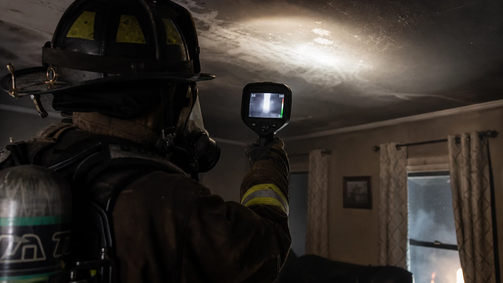 Photorealistic photo of a firefighter in structural turnout gear and SCBA using a thermal imaging camera to scan a residential ceiling for signs of attic fire &mdash; the TIC screen visible showing a bright white hot area across the ceiling plane indicating heat above, the firefighter scanning methodically in a smoke-filled interior room, realistic editorial fire service photography style