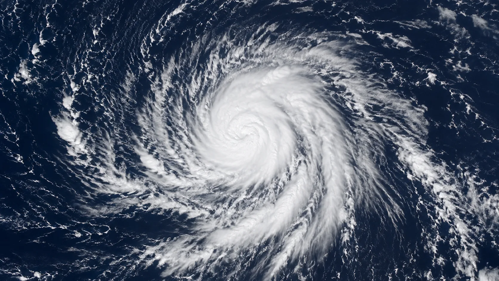 Satellite view of a swirling tropical disturbance over open dark blue Pacific Ocean water, organized cloud bands visible, no landmass in frame