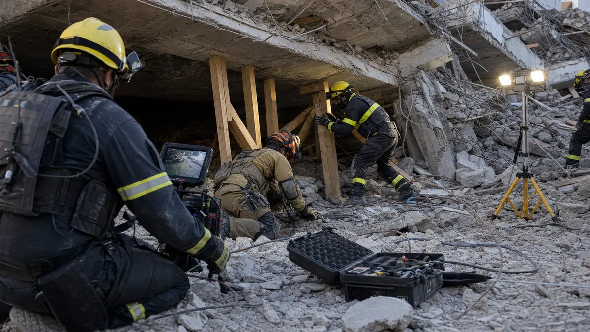Urban search and rescue firefighters setting shoring and using search equipment at a collapsed concrete structure.